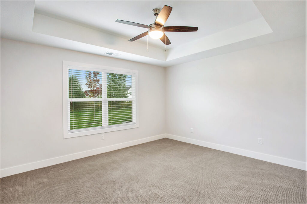 A carpeted bedroom with high ceiling and fan